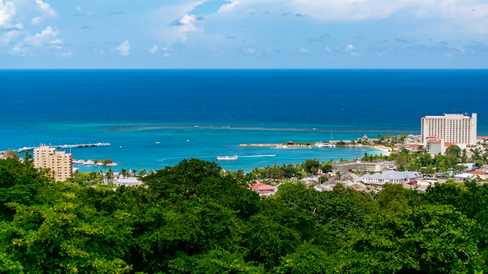 Aerial view of a Caribbean coastal town, turquoise water meeting a hillside community