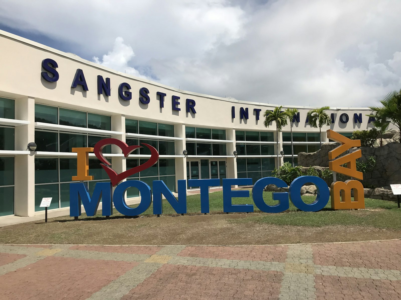 Large I Love Montego Bay letter sign on a lawn in front of the curved Sangster International Airport building